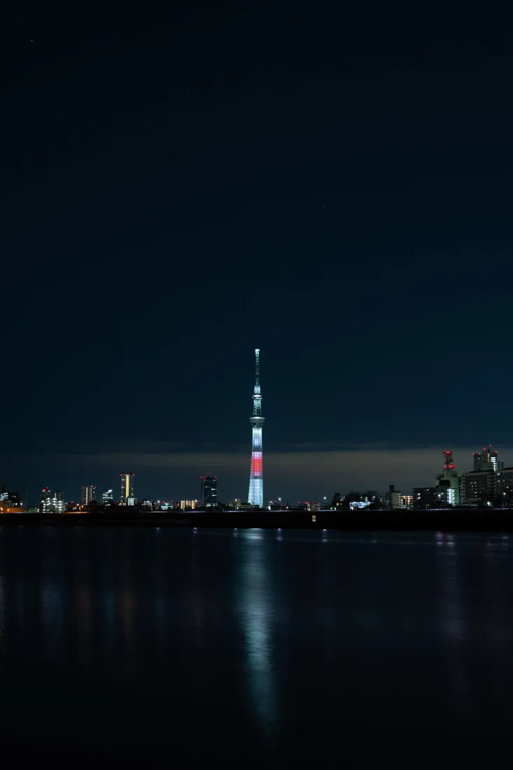 夜晚水岸前的城市天际线，中央亮灯高塔在水面投下清晰倒影