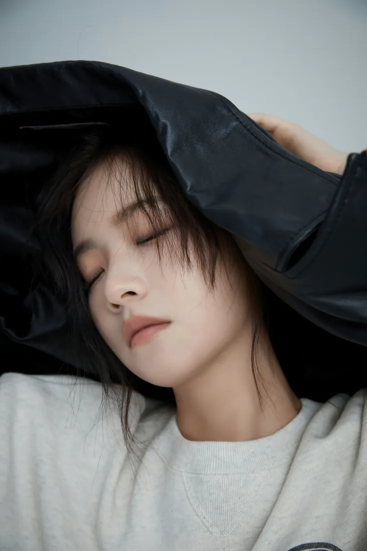 李庚希闭眼抬手将黑色外套搭在头顶，身着白色上衣，神态清冷随性。