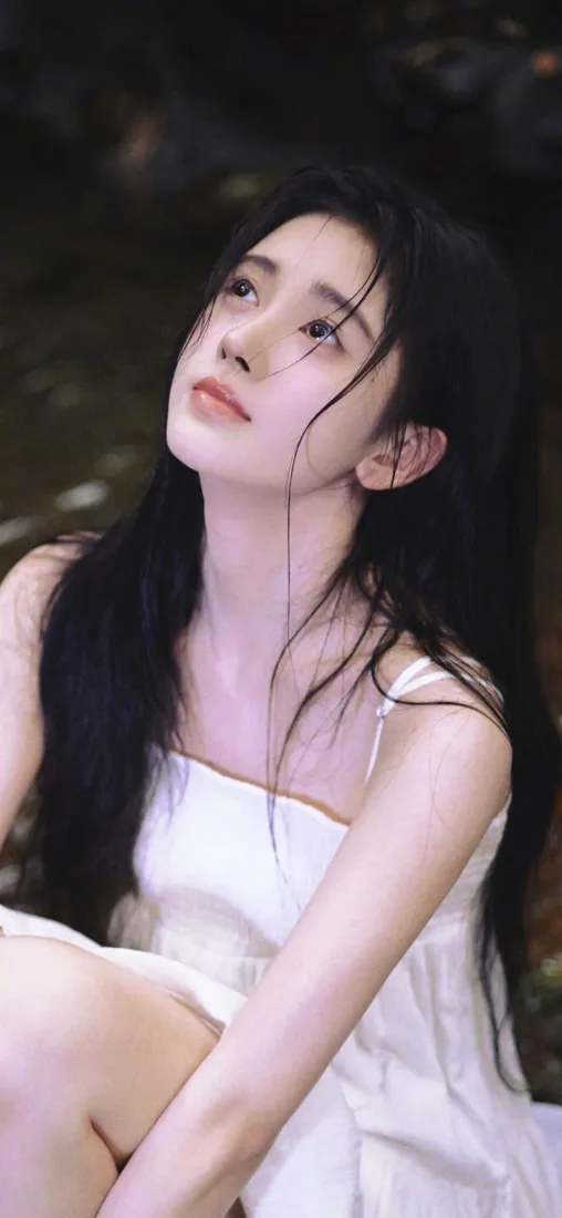 鞠婧祎身着白色吊带裙，黑长直发，林间仰头望向斜上方，背景虚化。