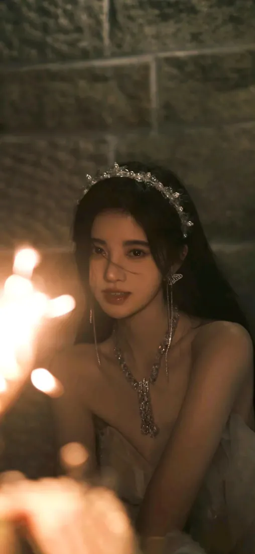 鞠婧祎佩戴镶钻发箍与流苏耳饰，手持发光仙女棒，石墙前朦胧暖调人像。