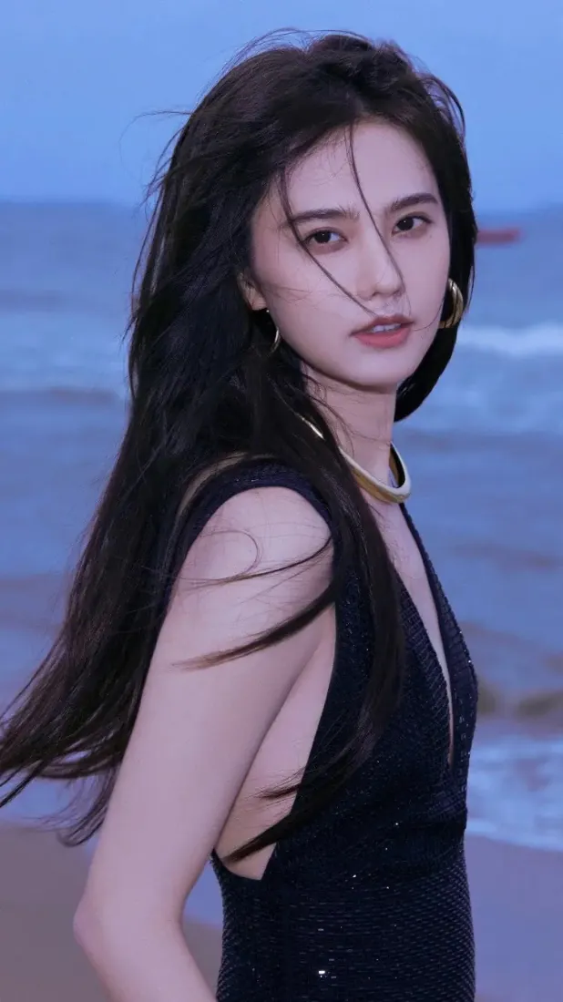 姜佩瑶身着黑色深V礼服，佩戴金色首饰，在黄昏海边回眸望向镜头