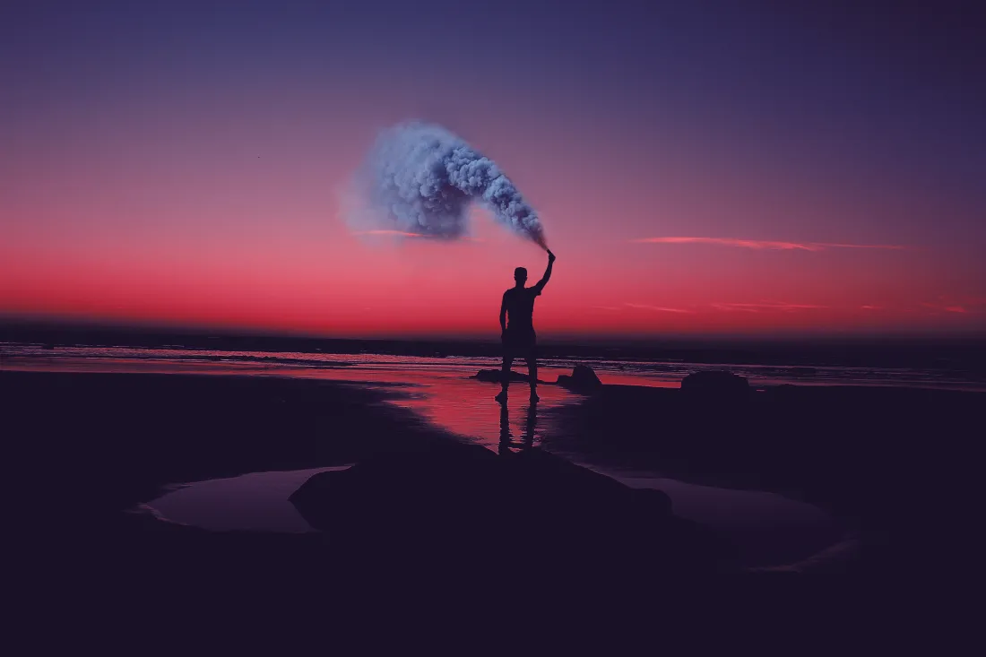 黄昏海边滩涂，人物剪影抬手释放烟雾，天空呈现紫到红的渐变。