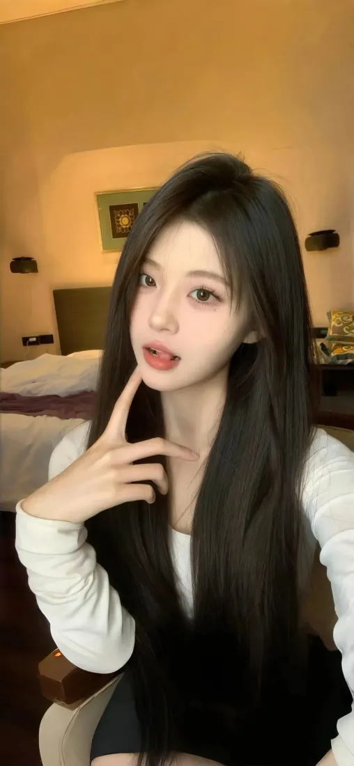 暖光酒店房间内，黑长直长发女生穿白色长袖上衣自拍，手托脸颊看向镜头。