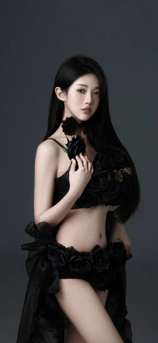灰调纯色背景前，长发黑衣女性手持黑玫瑰，姿态优雅性感。