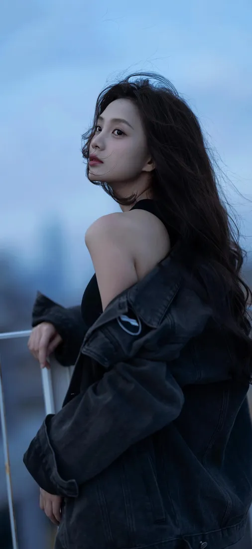 黄昏天台，黑衣长发女子倚栏回眸，背景虚化朦胧。