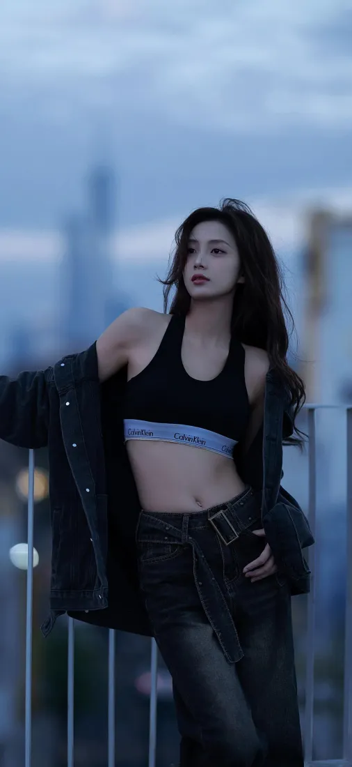 黄昏天台，长发酷感女生穿黑色运动内衣与外套，倚靠栏杆望向侧方。
