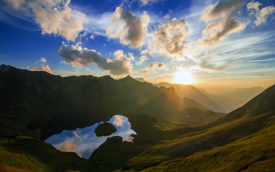 黄昏时分山谷湖泊倒映天空，远处山峦在夕阳下层次分明