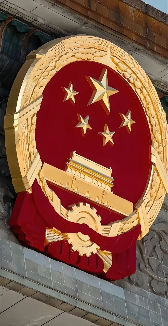 低角度拍摄的立体金色中华人民共和国国徽，红底配五星与天安门浮雕