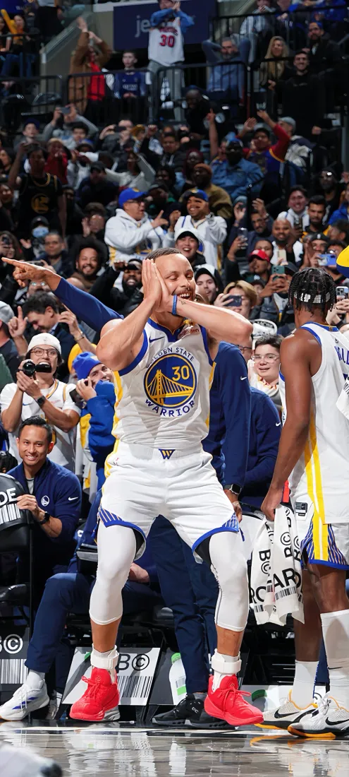 NBA球星库里身着勇士30号球衣在赛场边做出庆祝动作，身后是欢呼的观众。