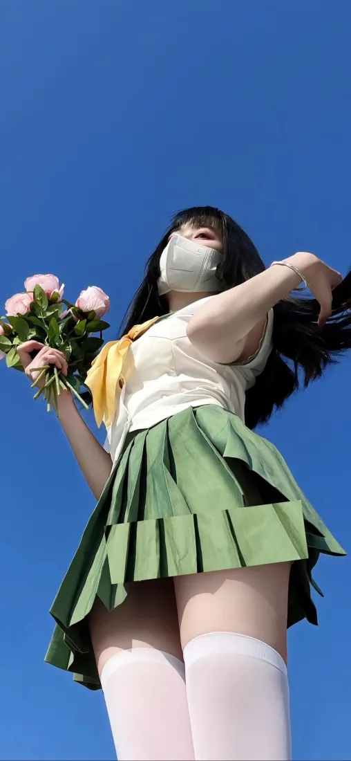 仰拍蓝天背景下，穿JK制服戴口罩的少女手持粉色花束站立