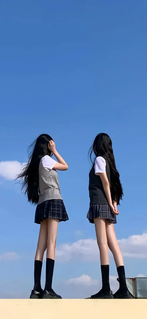两名身着JK制服的长发少女背对镜头立于澄澈蓝天之下，青春感十足