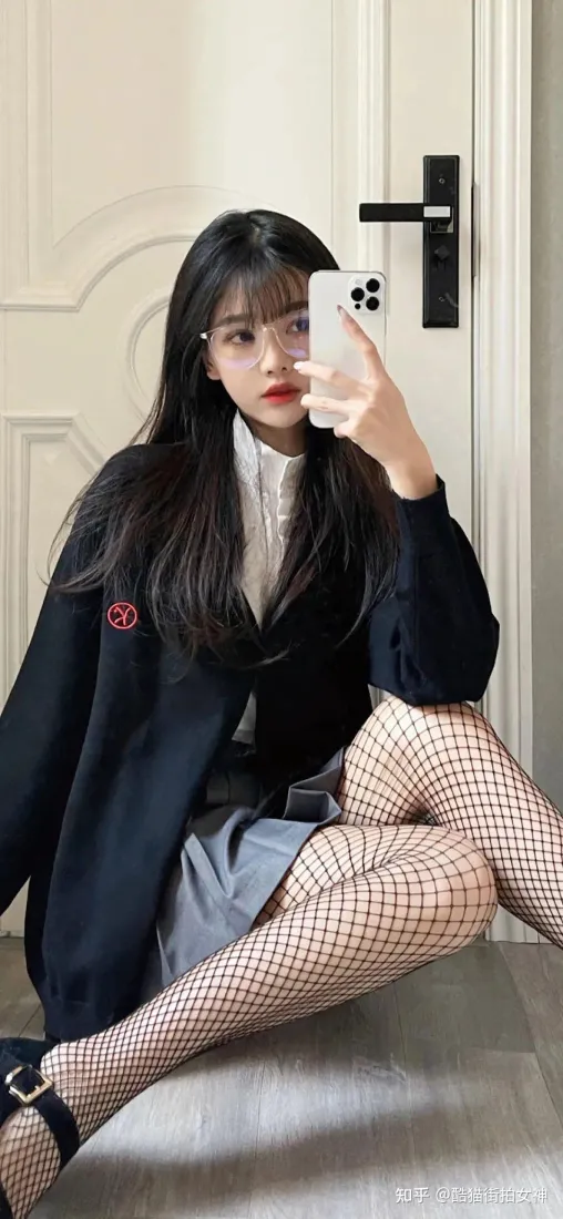 黑长直戴眼镜女生穿制服搭配渔网袜，坐于门前持手机对镜自拍