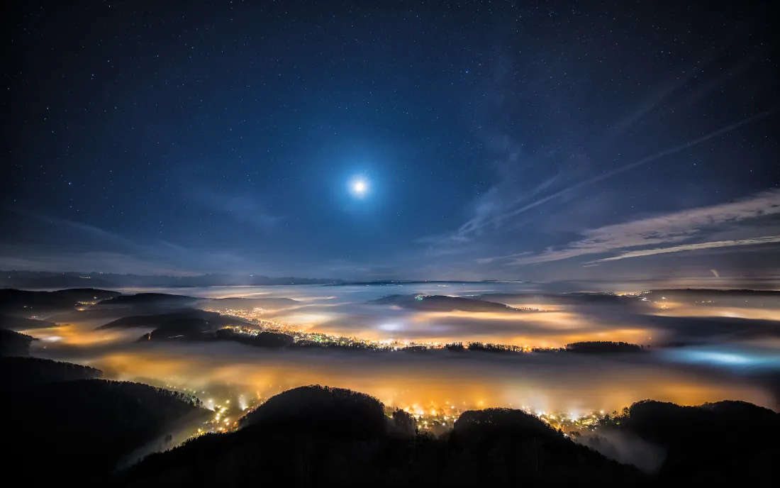 月夜下的山谷云海，城市暖光从云海中透出，远山剪影错落。