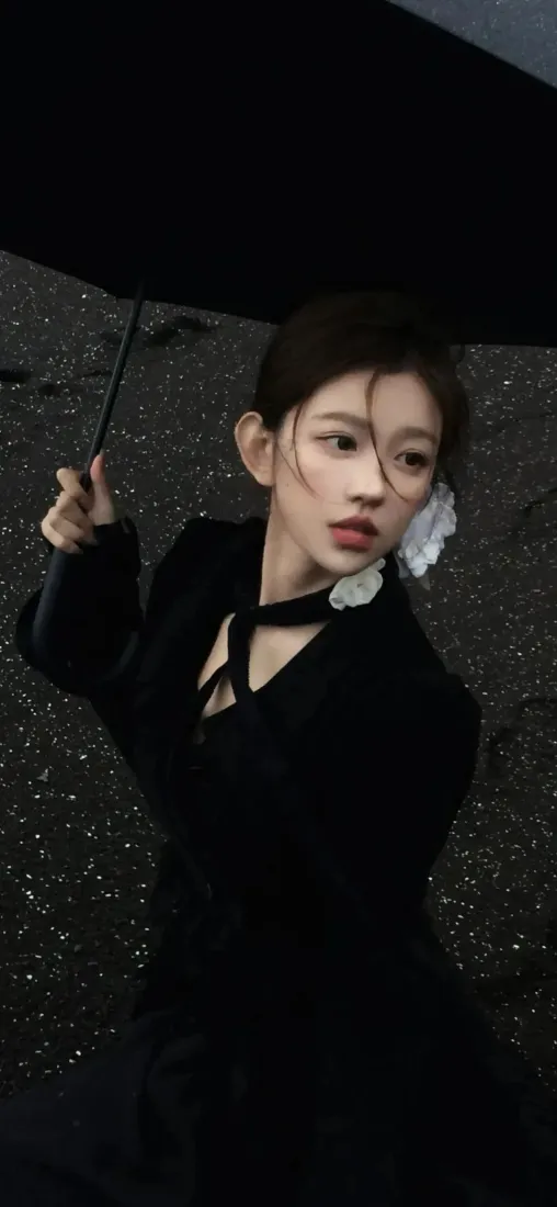 身着黑色服饰的年轻女子在雨中撑黑伞，侧头望向画面右侧。