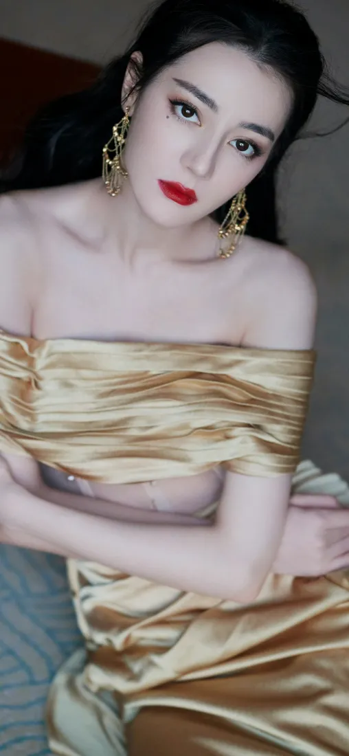 迪丽热巴身着金色抹胸礼服，佩戴华丽金耳饰，红唇妆容明艳动人。