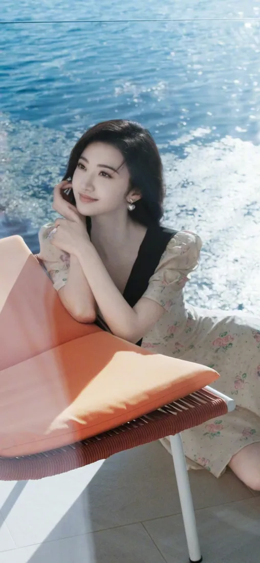 景甜身着碎花连衣裙倚靠在海边露台躺椅旁，背景是波光粼粼的蓝色海面。
