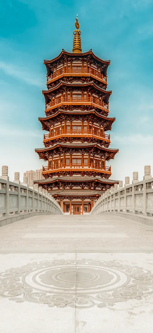石拱桥尽头矗立多层红棕色中式古塔，两侧石栏杆对称，上方是澄澈蓝天。
