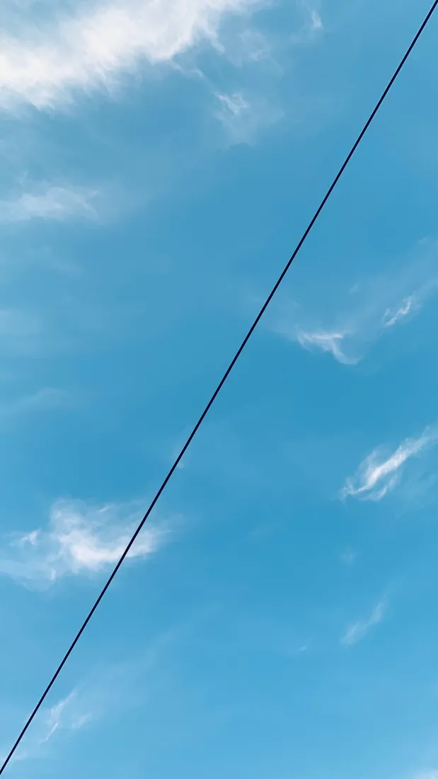 澄澈蓝天点缀细碎白云，一道黑色电线斜向贯穿画面。