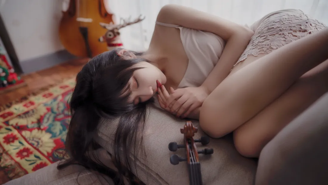 长发女子身着白色蕾丝吊带侧卧沙发休憩，身旁摆放小提琴，背景有大提琴与地毯。