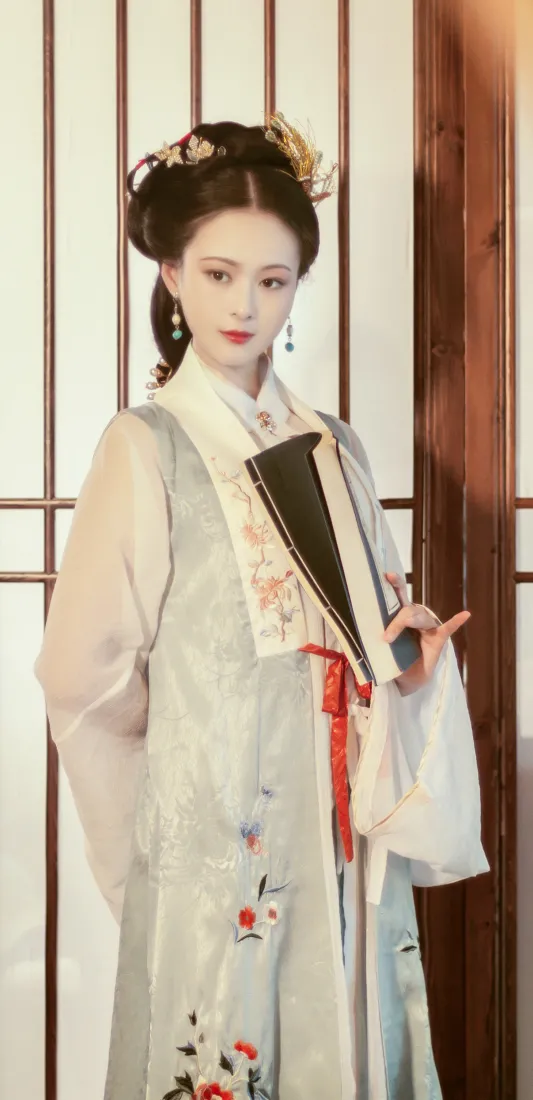身着浅灰绣花汉服的女子手持折扇，立于中式木格门前，气质温婉典雅。