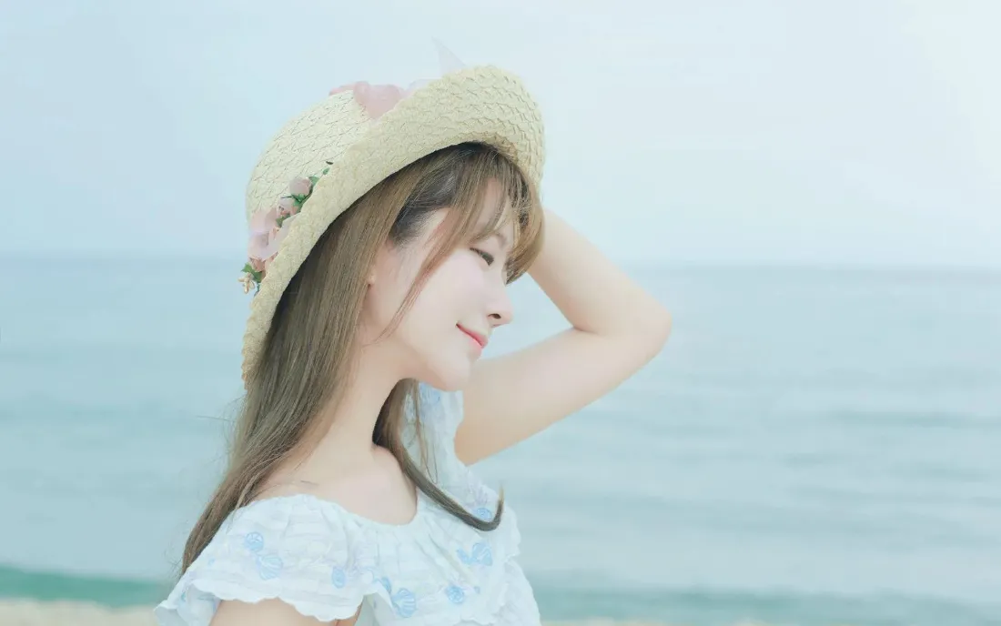 2k草帽美女壁纸|海边背景图片 - 魅力夏日「哲风壁纸」 戴装饰花草草帽的年轻女子在海边侧身抬手扶帽,闭眼浅笑,背景是淡蓝朦胧的海天。
