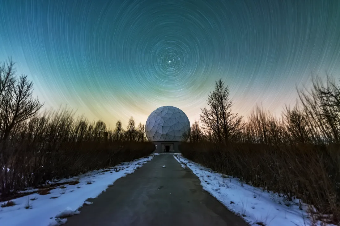 冬季残雪道路尽头的天文台圆顶，上方是螺旋星迹与渐变青蓝夜空