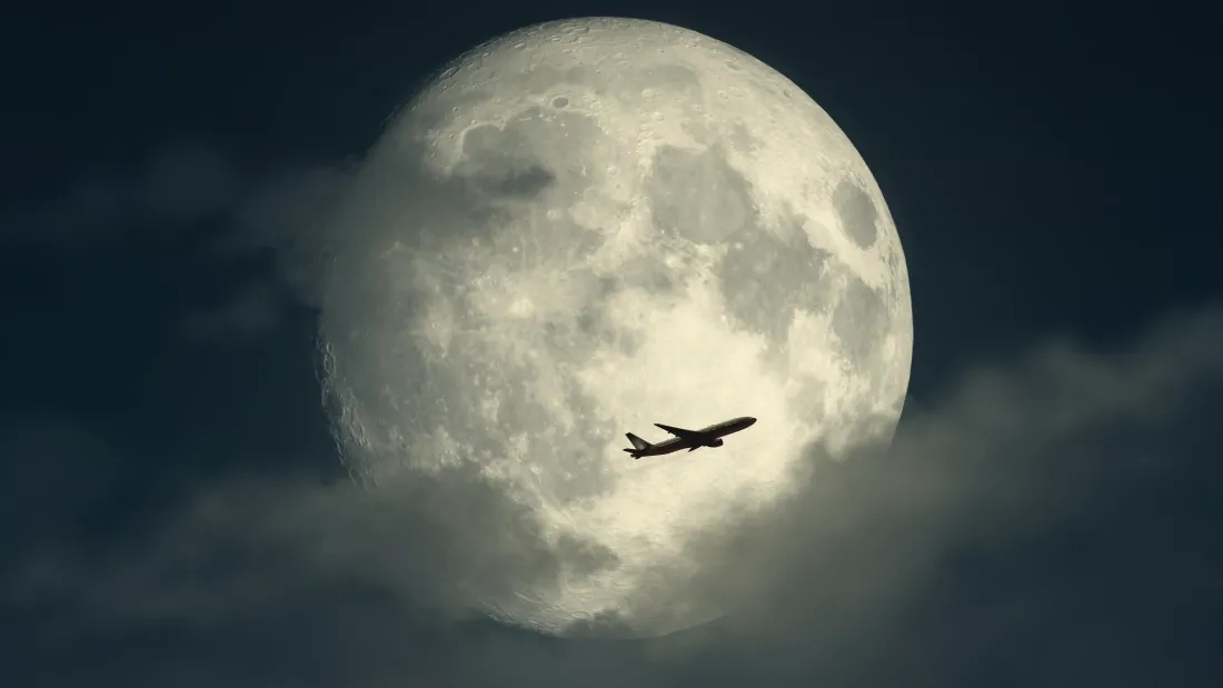 暗蓝夜空里巨大满月悬于中央，民航客机剪影从月面前方掠过，薄云轻绕月缘。