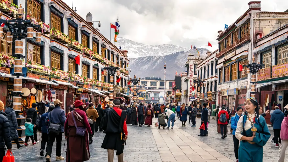 拉萨八廓街藏式商业街景，行人往来，远处可见雪山。
