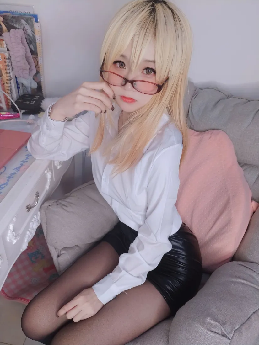 金发戴红框眼镜的女生穿白衬衫黑皮裙黑丝，坐在灰色沙发上扶眼镜。