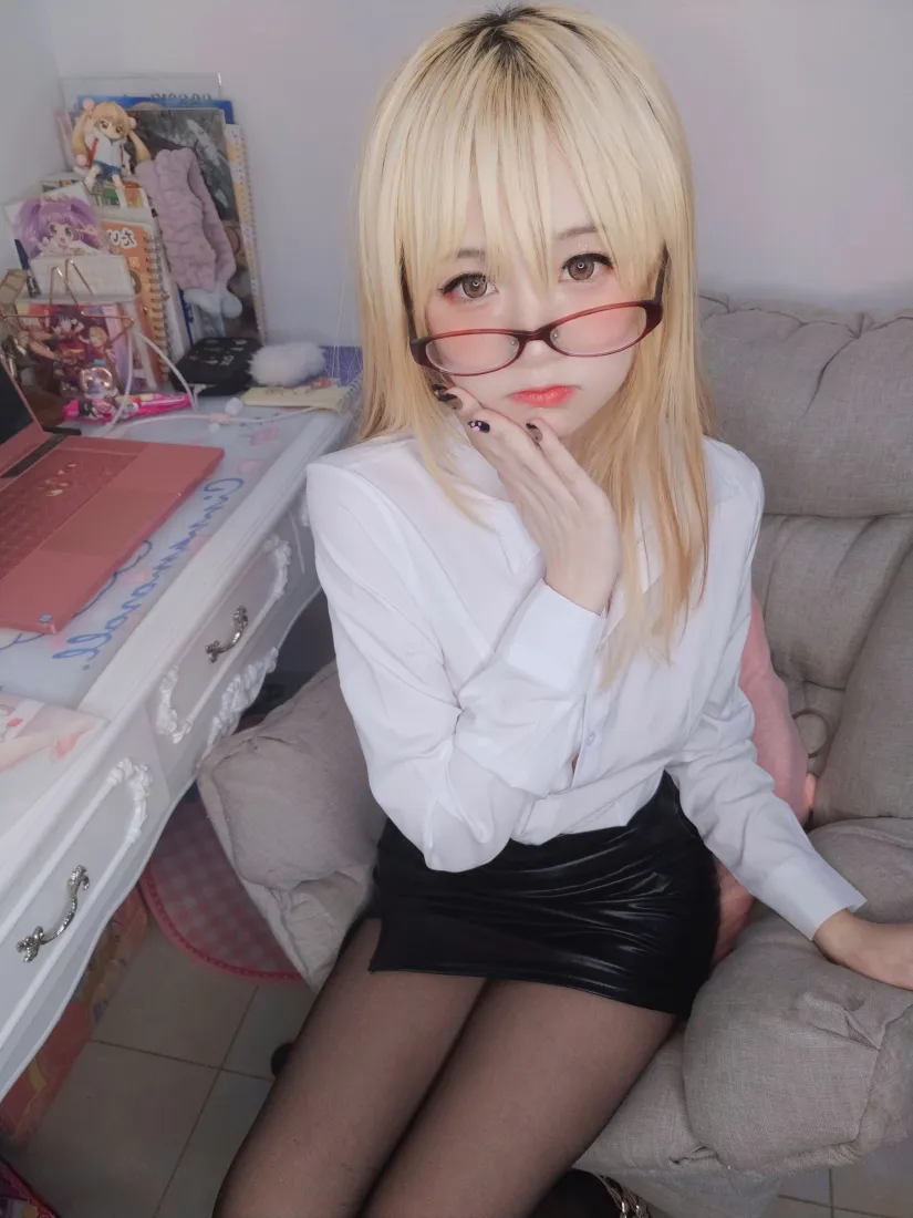 金发戴眼镜的女性身着白衬衫黑短裙黑丝，坐在室内沙发上托腮看向镜头