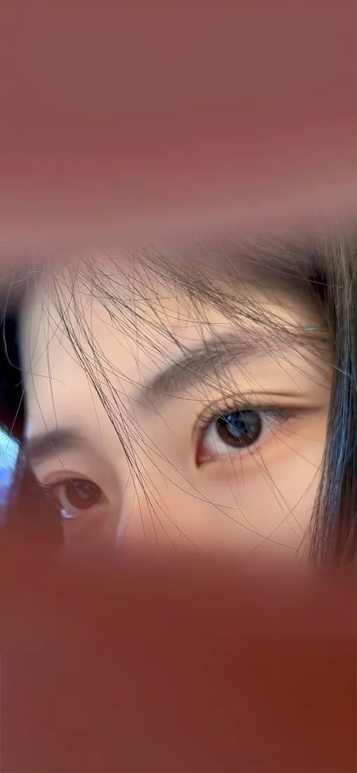 红色朦胧背景下的女性眼部特写，发丝轻拂眉眼，眼神柔和。