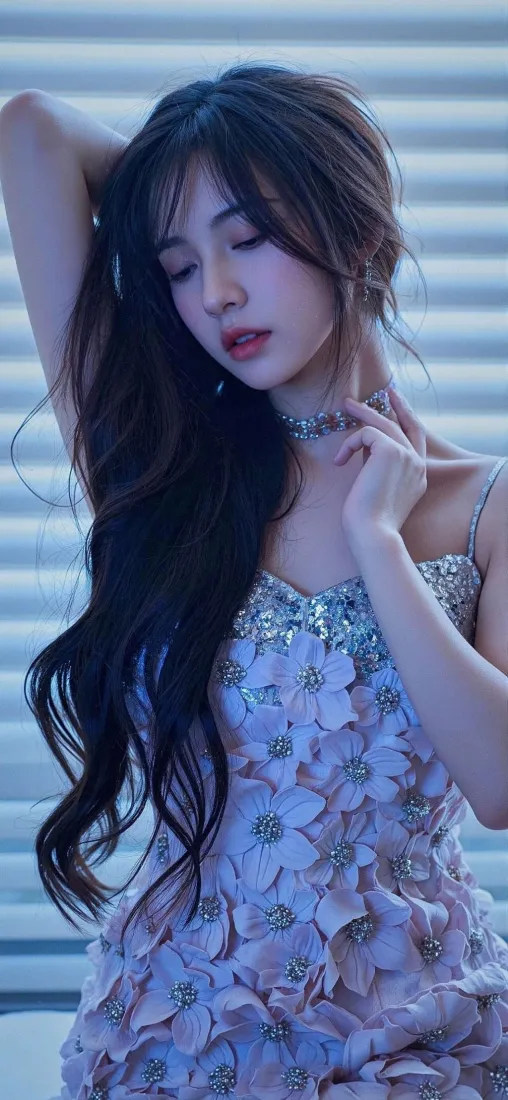 长发女子身着立体花瓣装饰的紫色吊带裙，闭眼抬手置于脑后，背景为横向百叶窗。