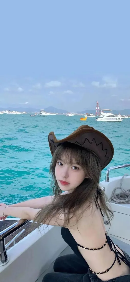 戴棕色牛仔帽的黑衣美女坐在游艇上，背景是碧海蓝天与远处的船只