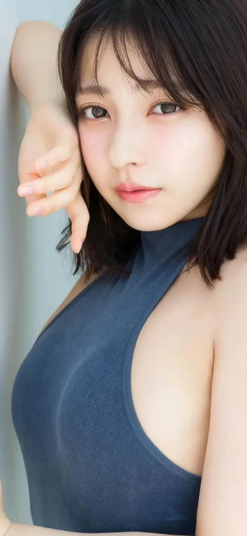 短发年轻女性身着深蓝色挂脖紧身衣，手轻靠头部，浅蓝纯色背景写真