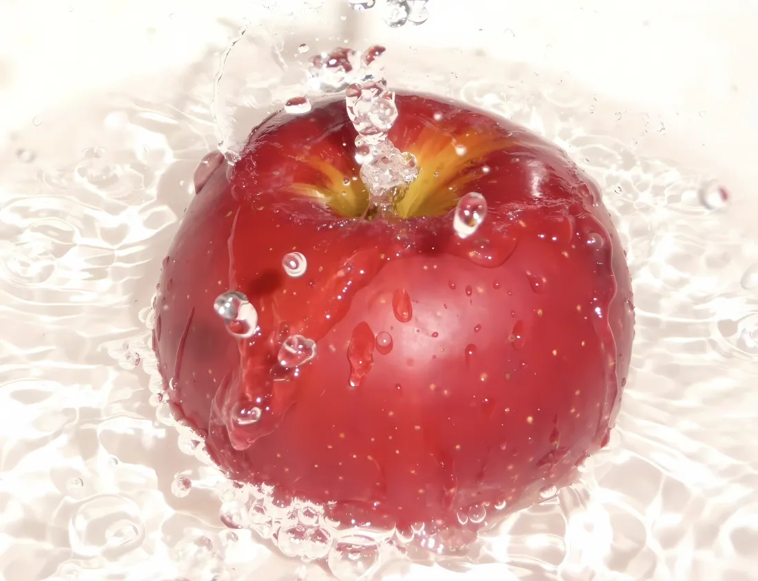 红苹果置于清透水中，水花飞溅，水珠附着在果面，背景明亮干净。