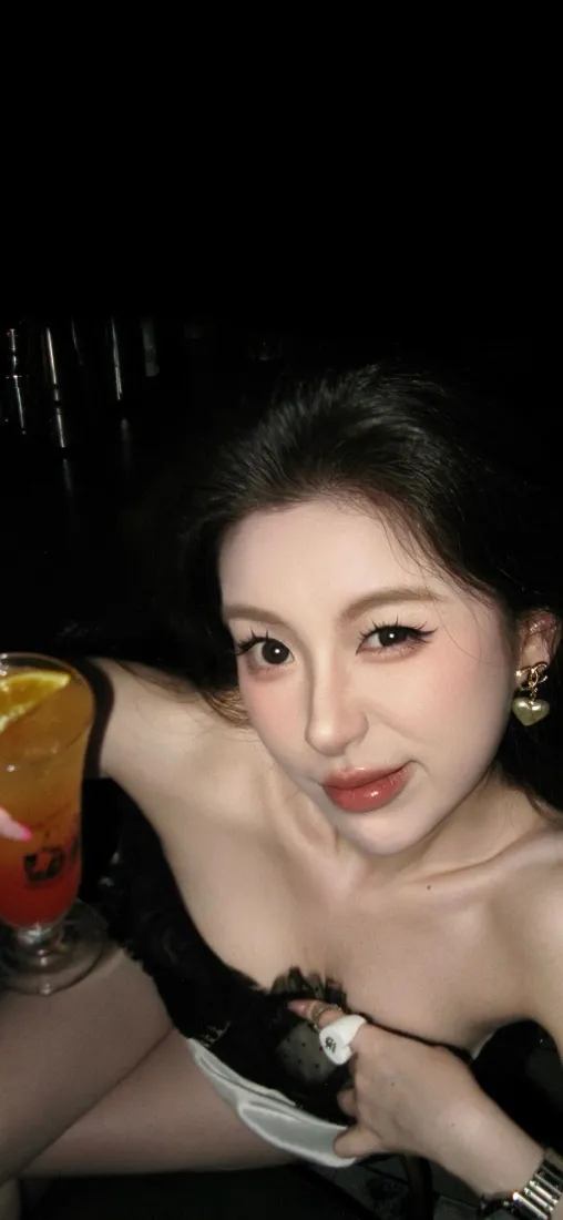 夜景中穿黑色抹胸的年轻女性手持渐变橙红色饮品自拍