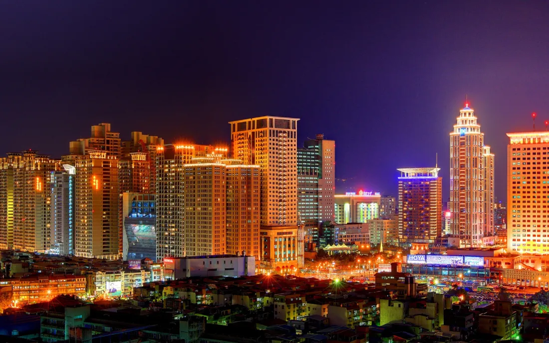 紫调夜幕下的城市天际线，连片高楼被暖橙灯光点亮，灯火璀璨。
