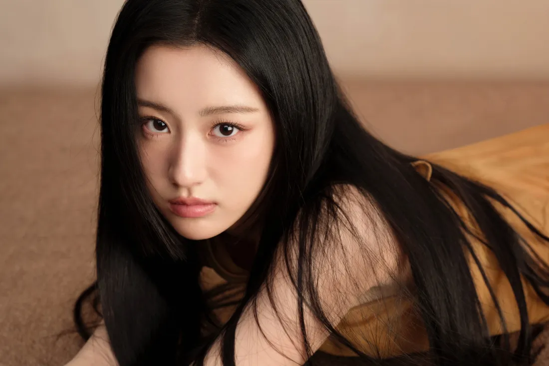 暖棕背景前，长发女性近景直视镜头，气质沉静。