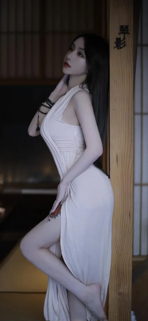 长发女子身着白色开叉旗袍，倚靠日式木质门框侧身摆拍。