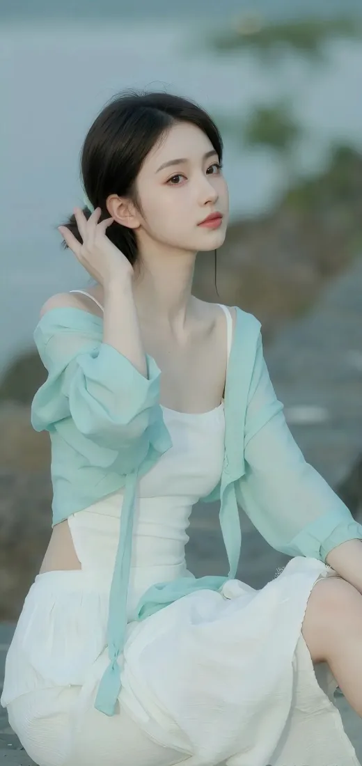 水边户外，身着白色吊带裙与浅绿薄衫的年轻女子侧身坐于岸边
