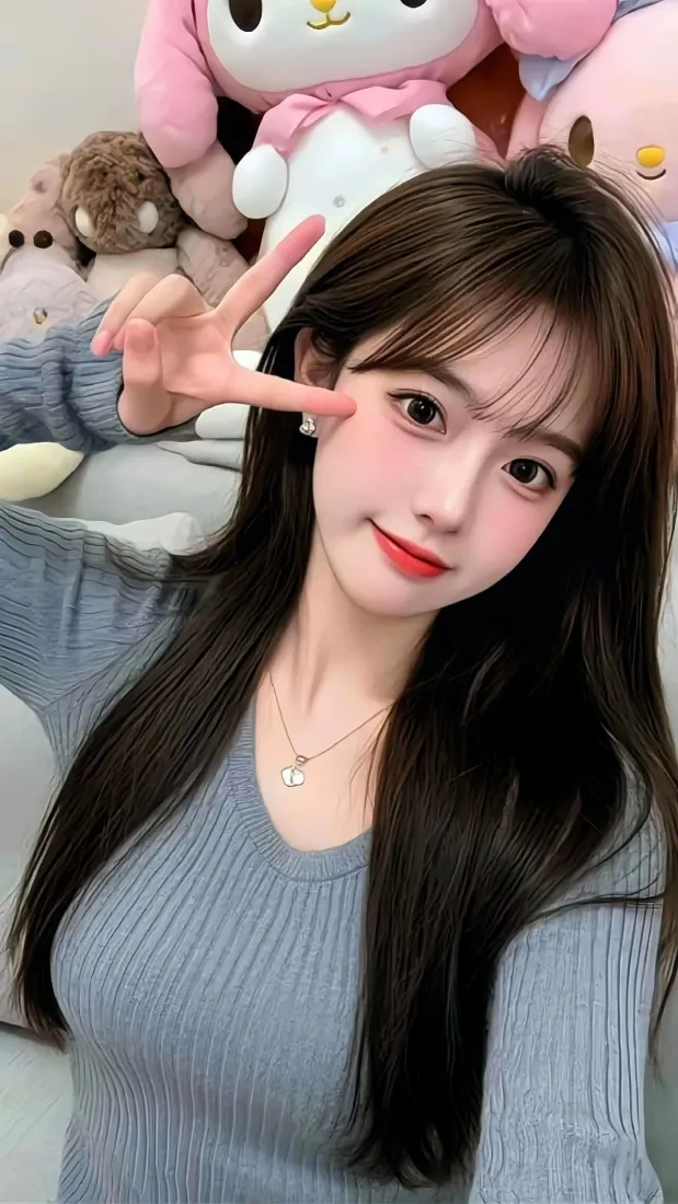 长发女生穿灰色针织衫，在玩偶背景前比耶自拍