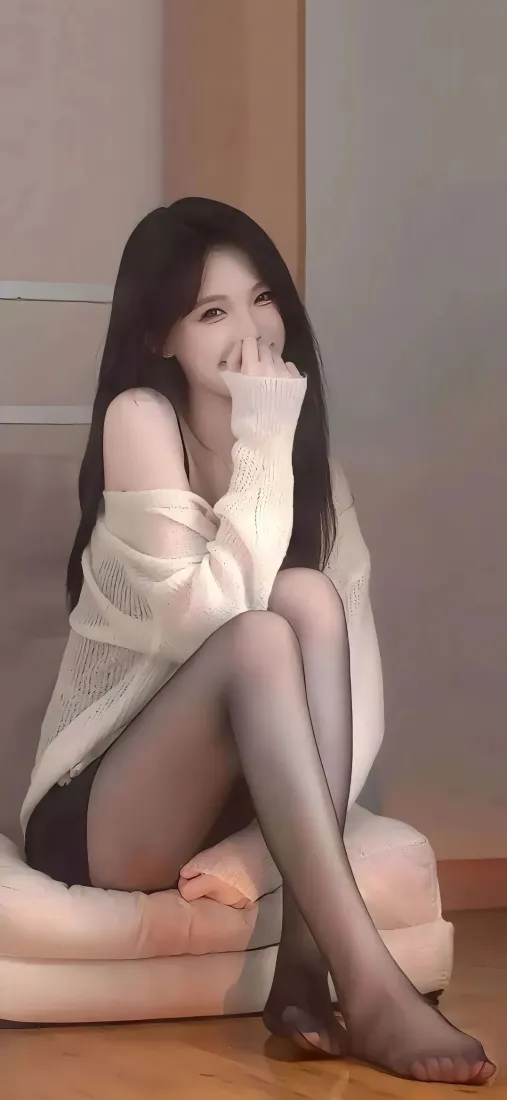 长发白衣黑丝女子坐于室内浅色沙发，手掩嘴微笑