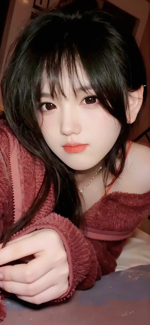 室内近景自拍，齐刘海黑长发年轻女生身着酒红色毛绒露肩上衣，妆容柔和。
