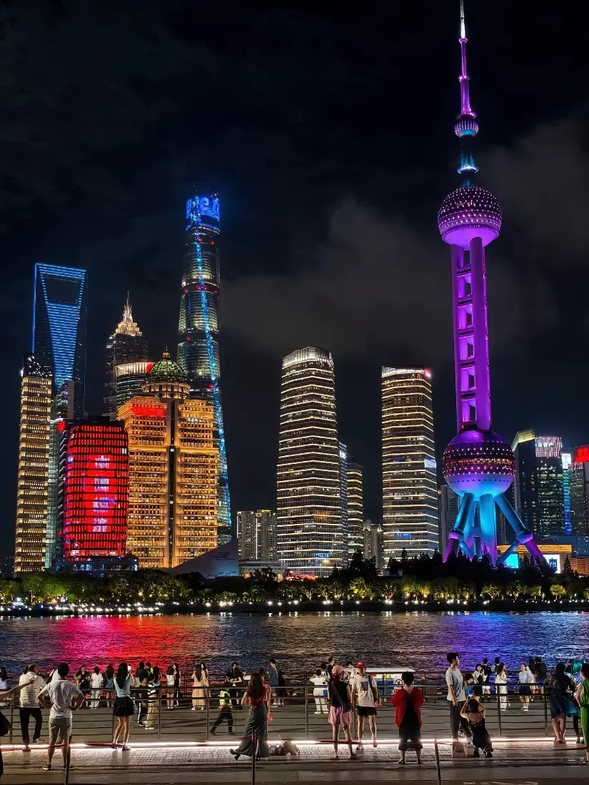 上海黄浦江畔夜景，东方明珠与陆家嘴摩天楼灯火璀璨，江畔人群观赏江景。