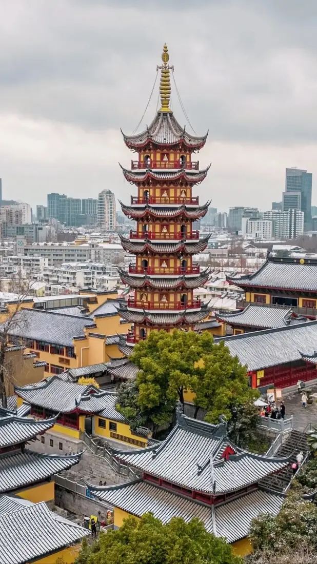 阴天俯瞰南京鸡鸣寺，覆雪黄墙灰瓦古建与远处城市天际线相映。