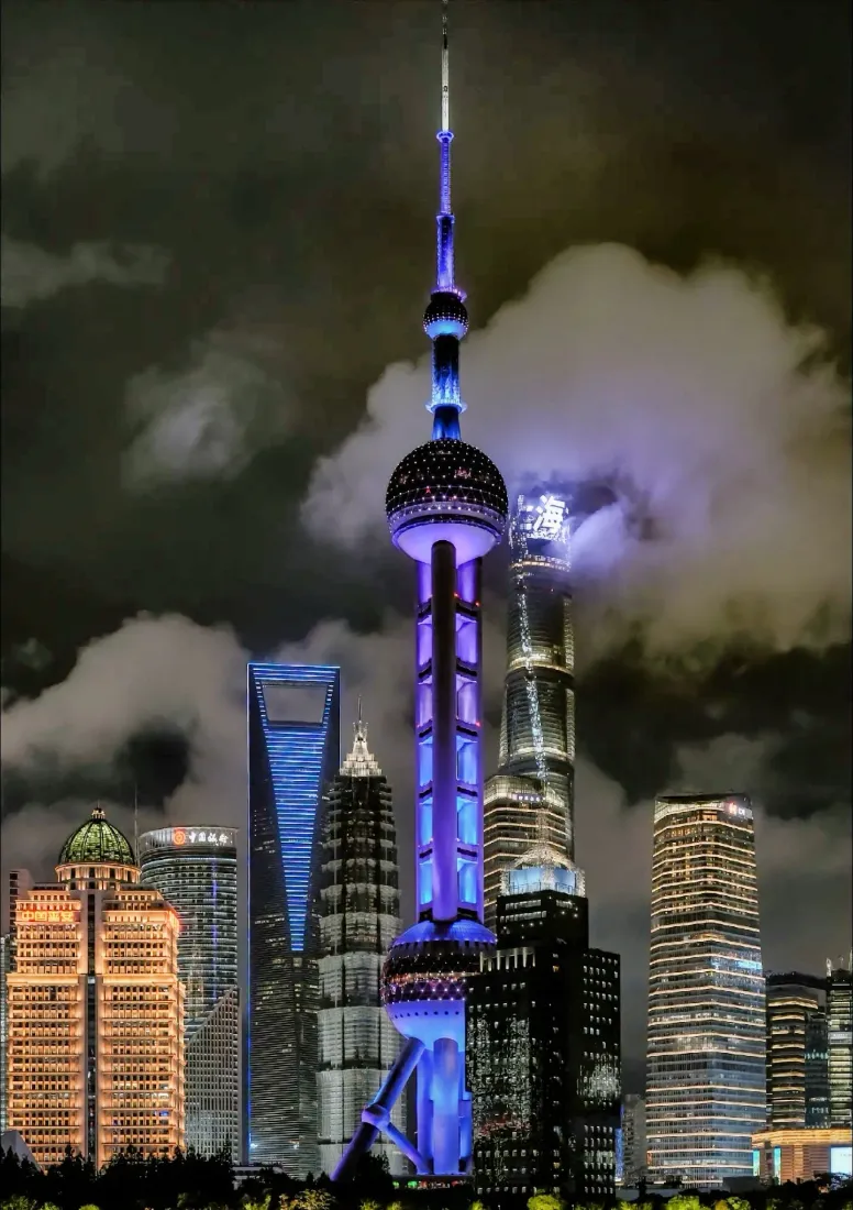 上海陆家嘴夜景，东方明珠亮紫蓝灯光，摩天群楼与云层交织。
