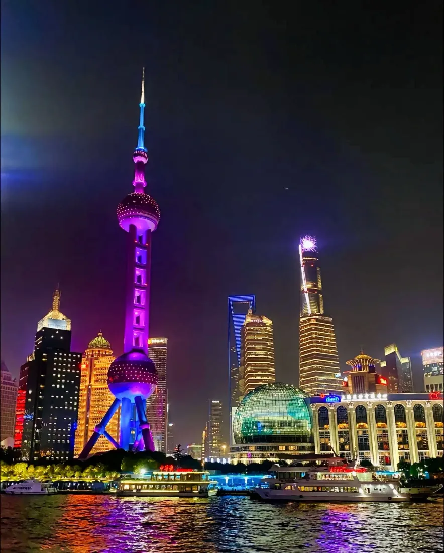 上海黄浦江畔夜景，东方明珠与摩天大楼灯光璀璨，江面倒映霓虹。