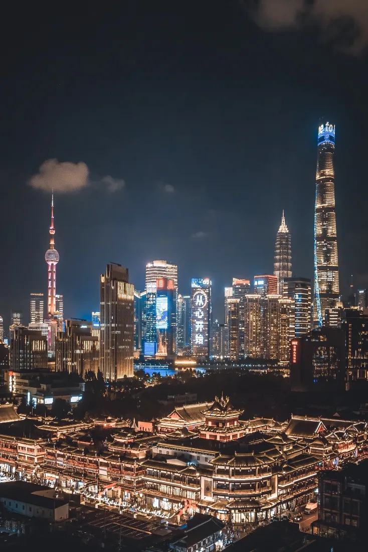 上海陆家嘴夜景，东方明珠与摩天楼灯火璀璨，前景是亮灯的中式传统建筑群。