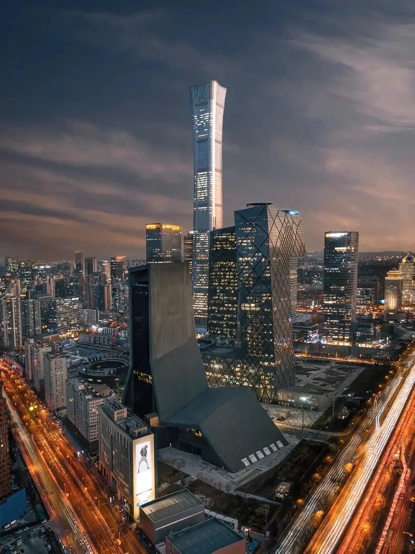黄昏入夜的北京CBD天际线，中国尊矗立中央，道路车流拉出暖光轨迹