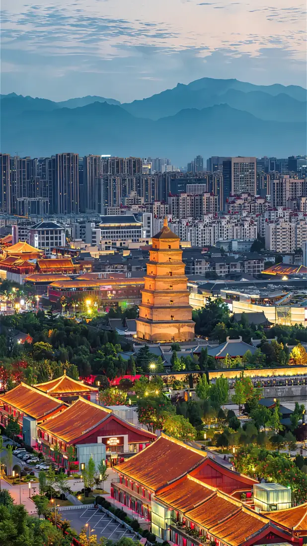 黄昏时分西安大雁塔矗立在城市中，周边红顶古建与现代楼宇相映，远山层叠。
